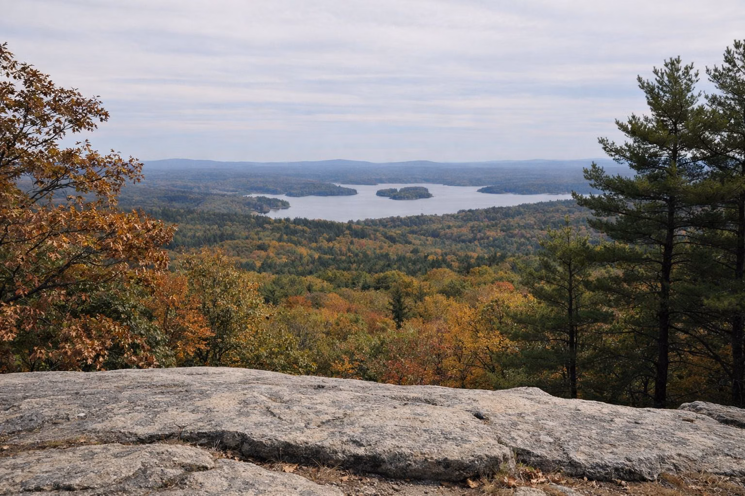 View from a rocky hilltop ledge over autumn forest to a distant lake with islands